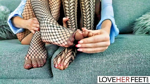 Skinny fair babe in fishnet stockings touches her red-pedicured toes on couch