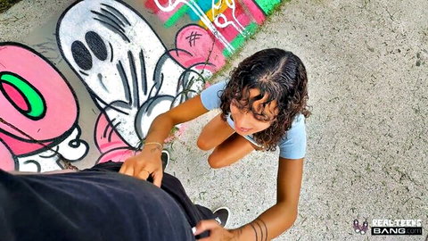Isabella Jules kneels teasing Alex Jett outdoors by graffiti