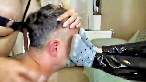 Dominatrix shoves blue polka-dot socked foot into submissive man's mouth while exposing big bare tits