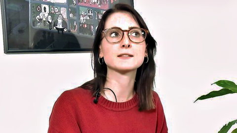 Brunette woman with glasses smiling in red sweater by plant