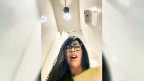Latina with glasses in yellow top opens mouth wide behind shower curtain