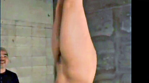 Nude woman suspended upside down in bondage with legs spread exposing pussy and asshole to smiling man