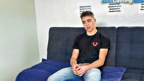 Nervous athletic guy in black True Religion tee and jeans sits for muscular neighbor audition casting couch