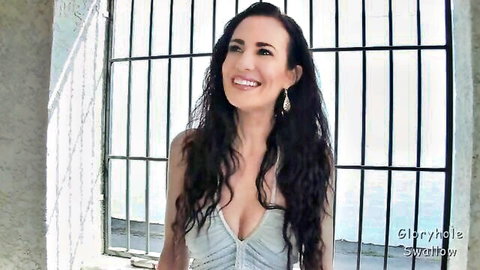 Seductive brunette cougar smiles through glory hole teasing deep cleavage for cock