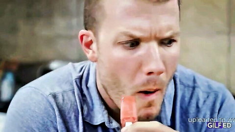 Buzzcut man sensually sucking thick pink popsicle with wide eyes and open mouth in kitchen