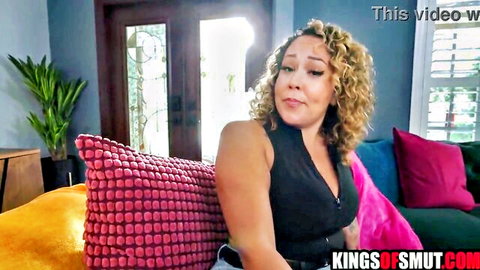 Curly haired MILF teases deep cleavage in tight black tank top on couch