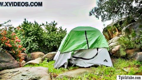Green tent pitched in scenic outdoor camping spot with rocks and lush greenery for hot tgirl adventure