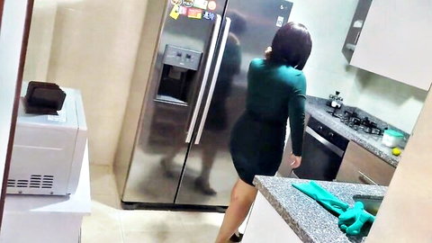 Curvy MILF in tight green dress teasing from behind in kitchen