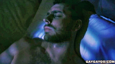 Hoss Kado shirtless in bed, eyes closed, bearded muscular man