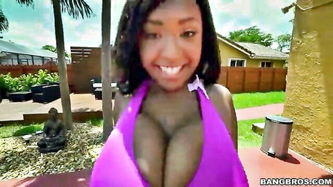 Curvy ebony babe smiling with huge tits bursting from tight purple bikini by pool