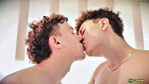 Two curly-haired young men passionately kissing shirtless in intimate embrace