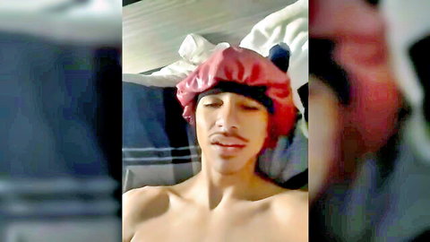 Ebony guy in red shower cap lying shirtless on bed smirking seductively