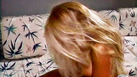 Blonde with long wavy hair turned sideways nude on tropical palm pillows teasing viewers