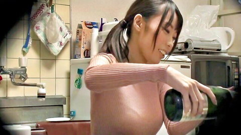Amateur Asian wife in pink sweater pouring wine in kitchen, teasing smile