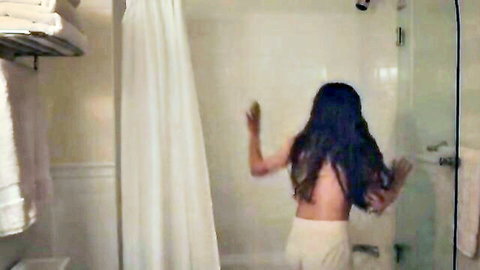 Topless woman with long dark hair stands bare-backed in white panties turning on shower in bathroom