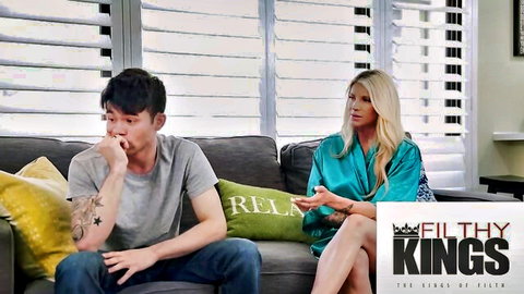Blonde MILF in open teal satin robe teases cleavage with tattooed Asian guy on couch