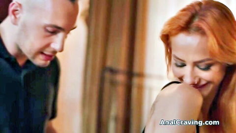 Redhead woman laughing flirtatiously with bald man in black dress