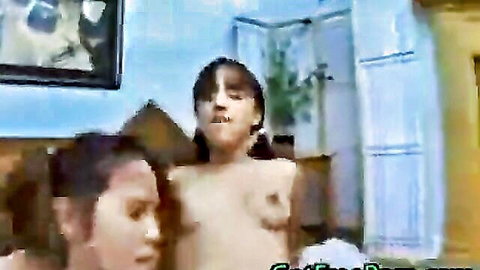 Two topless women, one looking at the camera, possibly in a bedroom