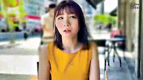 Cute Asian babe with bangs in tight yellow top sitting at outdoor cafe