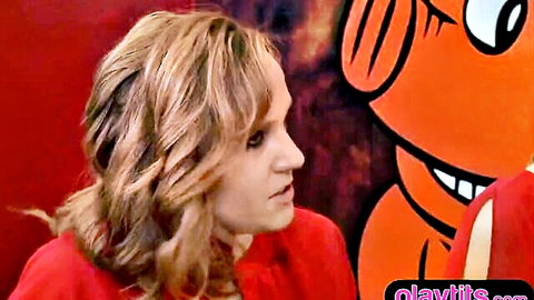 Blonde woman in red dress looking sideways near orange cartoon mascot