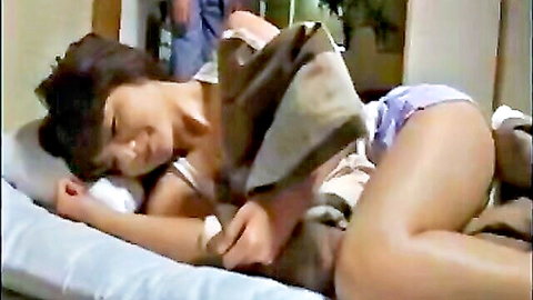 Asian woman in tank top and shorts lounging on bed with man nearby