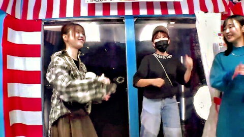 Three smiling East Asian girls in casual clothes dancing with pompoms at a striped festival booth