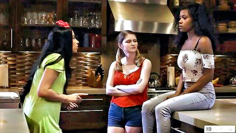 Three clothed women chatting in kitchen, green dress babe pointing at red top hottie and white top sitter