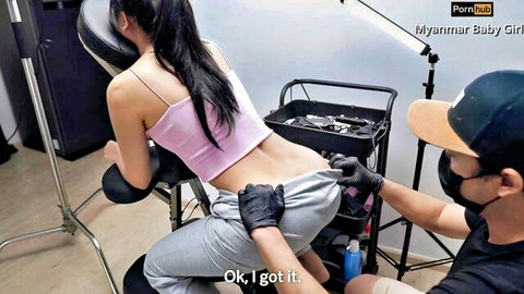 Gloved Asian masseur pulls down Myanmar girl's gray sweatpants exposing her big bare ass on massage table