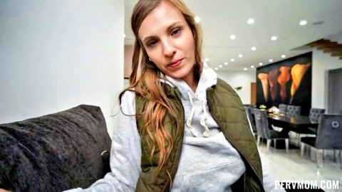 Redhead MILF in gray hoodie and green vest sitting on couch smiling seductively
