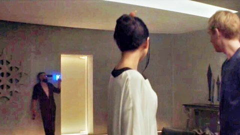 Sensual Asian woman in white blouse stands between blond hunk and shirtless man in artistic room