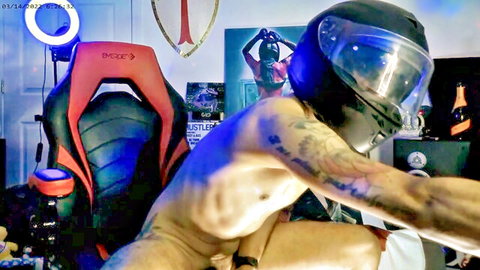 Tattooed muscular man in helmet sits naked in gaming chair exposing erect cock
