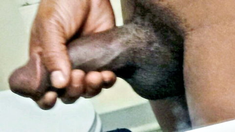 Close-up of black hand gripping large erect penis, explicit solo view