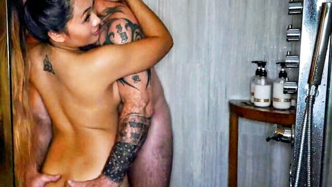 Tattooed Asian babe naked in shower embraced from behind by inked muscular guy groping her bare ass