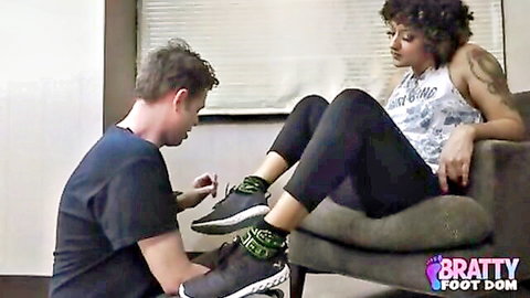 Kneeling man worships tattooed brunette's green sneaker foot in bratty foot dom session