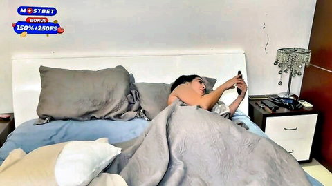 Sarah Black, curvy Latina model nude in bed, teasing with phone selfie