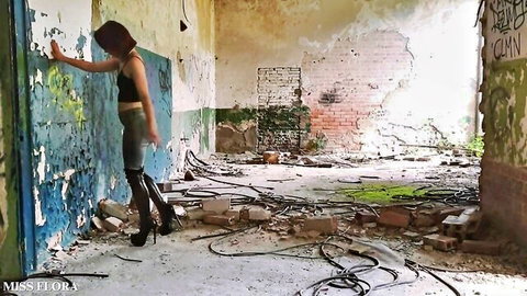 Brunette in tight jeans and high black boots teasing against graffiti wall in abandoned building