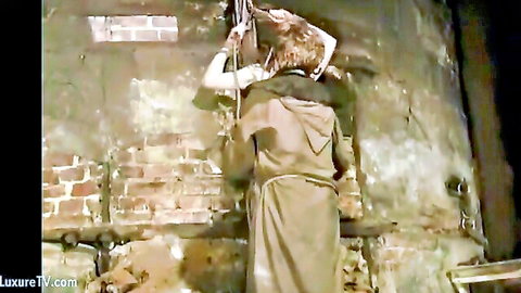 Hooded BDSM slave in pet hood suspended by bound wrists against brick dungeon wall
