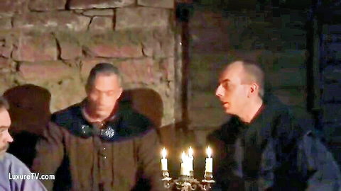 Three clothed dominant men in medieval attire sit at candlelit table in dimly lit stone room for BDSM slave scenario