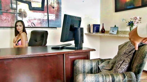 Kristina Rose in pink lingerie at office desk, intense gaze and foot play tease
