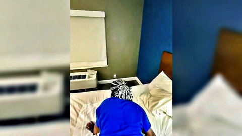 Black woman with dreads in blue shirt bent over bed, amateur tease