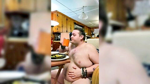 Chubby naked man with hairy belly sits at kitchen table holding drink exposing his nude body amateur solo