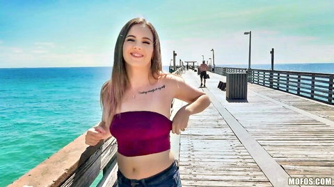 Skinny teen babe with tattoo smiling in purple tube top on beach pier by ocean