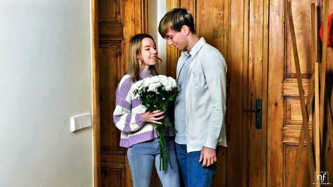 Skinny blonde teen in sweater holding flowers with boyfriend at door