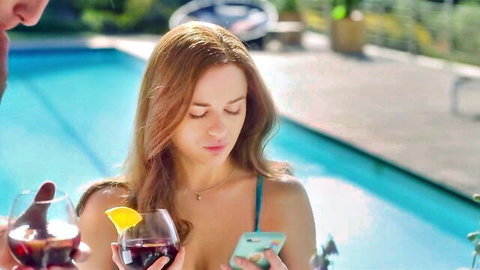 Joey King in sexy blue bikini by pool, holding wine glass and phone