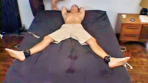 Bound athletic man in shorts, legs spread wide for intense tickle session