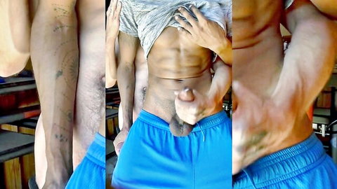 Tattooed muscular guy lifting shirt and stroking cock in blue gym shorts