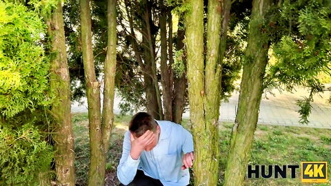 Embarrassed man covering face kneeling in lush green bushes outdoors