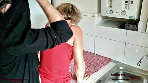 Blonde MILF in red tank top bent over kitchen sink grabbed by man behind ready for rough fuck