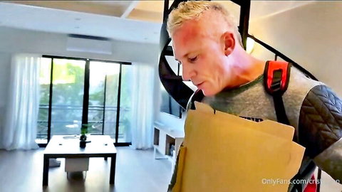 Muscular blonde hunk in tactical gear holding brown envelope in luxury apartment