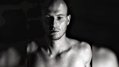 Bald muscular man topless in dramatic black and white portrait showing ripped chest and shoulders